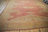 Long perspective of a distressed Oushak carpet with a faded cochineal red field and gold medallion.