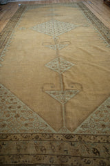 Angled view of the distressed Malayer carpet's central diamond medallion chain on a camel field.