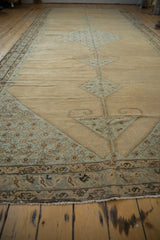 Angled view down the length of an antique Malayer carpet, detailing the worn texture and blue geometric corner.