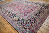 Wide navy floral border contrasting the scrolling magenta arabesque field of an antique carpet.