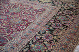 Low pile showing the antique Meshed carpet's magenta field beside its wide navy blue floral border.
