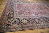 Angled perspective of an antique Persian carpet's wide, dark floral border and magenta arabesque field.