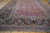 Angled view of an antique Meshed carpet's dramatic navy border and magenta scrolling floral field.