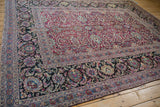 High corner view of an antique Meshed carpet's wide dark border and scrolling magenta field.