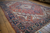 A vintage Heriz carpet from an angled perspective, showing the rich red field and detailed navy border.