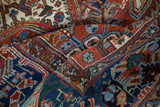 Folded vintage Heriz carpet showing the textured wool pile and arabesque floral motifs in red, blue, and sand.