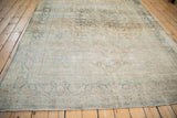 Angled view of a distressed antique Kerman carpet with a soft patina and faded floral medallion design.