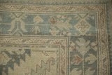 Worn hand-knotted pile on the vintage Oushak carpet's pale seafoam and beige border.
