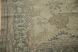 Distressed Oushak corner showing hand-knotted texture and a soft sea foam green border design.