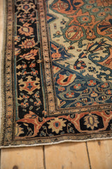 Corner view of an antique Farahan Sarouk rug showing its navy blue palmette border against an ivory field.