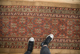 Antique Serab runner's brick red field with stylized geometric patterns, camel border, and sneakers.