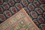 Folded corner of antique Persian rug showing navy boteh field and deep green border reverse.