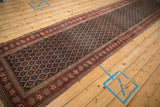 Long diagonal view of an antique Persian Bijar runner's navy lattice field and red vine border.