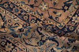 Antique Kerman carpet: dusty coral field, navy blue arabesques, varied pile texture.