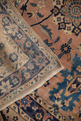 Antique Kerman carpet's folded corner displays dusty rose palmettes, navy vinery, and fringe.