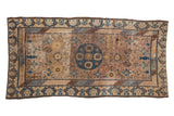 Distressed Khotan rug with prominent cobalt blue medallion, geometric designs, and muted mauve hues.