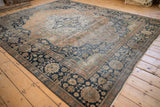 Angled view of an antique Mohtashem Kashan carpet highlighting its faded rust field and deep navy border.
