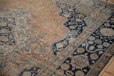 Corner view of an antique Kashan rug with a navy spandrel and vinery against a faded rust field.