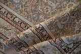 Folded antique Distressed Malayer rug showing geometric Herati design in dusty tones.