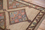 Detail of a hand-knotted diamond medallion and serrated leaf border on a beige lattice field.