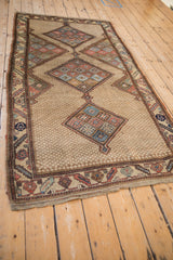 Angled view of an antique Persian rug with a triple diamond medallion and unidirectional prayer design.