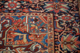 Corner detail of a vintage Heriz carpet showing geometric vines and blossoms in brick red, orange, and blue.