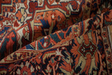 Folded vintage Heriz carpet showing its dense pile with geometric motifs in tangerine, red, and navy blue.