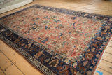 Angled view of an antique Lilihan carpet's allover floral design in copper and navy blue.