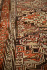 Angled view of the serrated vine border and rust-colored guls on a vintage Kurdish rug.