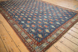 Distressed Kurdish carpet's geometric trellis pattern and floral border, seen from an angle.