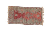 Antique Oushak rug mat with a ruby red diamond medallion on a faded seafoam green and mauve floral field.