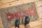 Antique Turkish Oushak rug mat shown for scale, displaying its faded ruby and seafoam green colors.