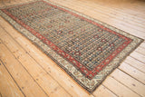 Antique Persian Qashqai runner from an angle, showing its repeating floral pattern and red borders.