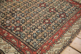 Antique Qashqai rug corner displaying a low pile texture, charcoal floral field, and madder red main border.