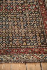 Corner view of an antique Qashqai rug, detailing the madder red border and low-pile floral field.