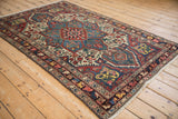 Vintage Persian Baktiari rug with a starburst medallion and wide floral border shown at an angle.