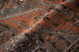 Curled section of Hamadan rug with textured pile, showing distressed chestnut, rust, and silver tones.