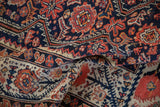 Textured close-up of a folded antique Malayer carpet with scrolling medallions in cobalt and madder red.