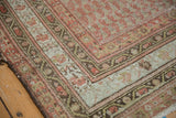 Corner of antique Malayer rug, showing faded ruby red field and ornate vine patterned borders.