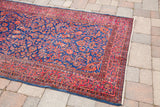Antique Kashan rug displaying royal blue and rich red floral motifs with visible white knots.