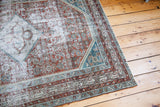 Distressed Malayer rug corner with faded tribal patterns in silver, teal, and red.