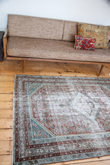 Corner of distressed Malayer rug with faded red, silver, and teal geometric border patterns.