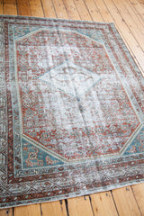 Distressed Malayer rug corner with faded terracotta, teal, and silver geometric patterns.