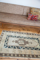 Geometric vintage Oushak rug with central cross motif and borders in muted beige and dark blue.