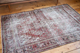 Distressed Joshegan rug border, its threadbare texture revealing faded red and dark tones.