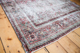 Edge of distressed Joshegan rug, showing threadbare texture and faded red, green pattern.