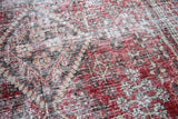 Threadbare texture on the vintage Joshegan rug with intricate red, light, and dark patterns.