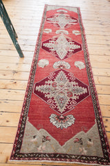 Vintage Oushak runner's soft cranberry red field, silver spandrels, meandering leaf borders, and fringe.