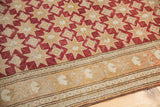 Corner of vintage Oushak rug displaying cranberry red geometric stars and stylized bronze border.