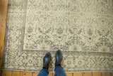 Distressed Oushak carpet close-up with feet, showing pale ivory field and earth-tone patterns.